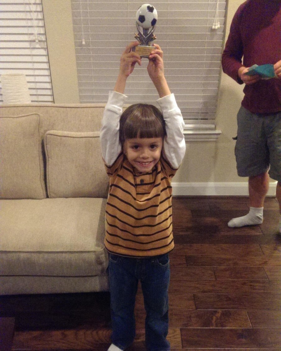 Young Lucas Weatherwax holding up a soccer trophy at home
